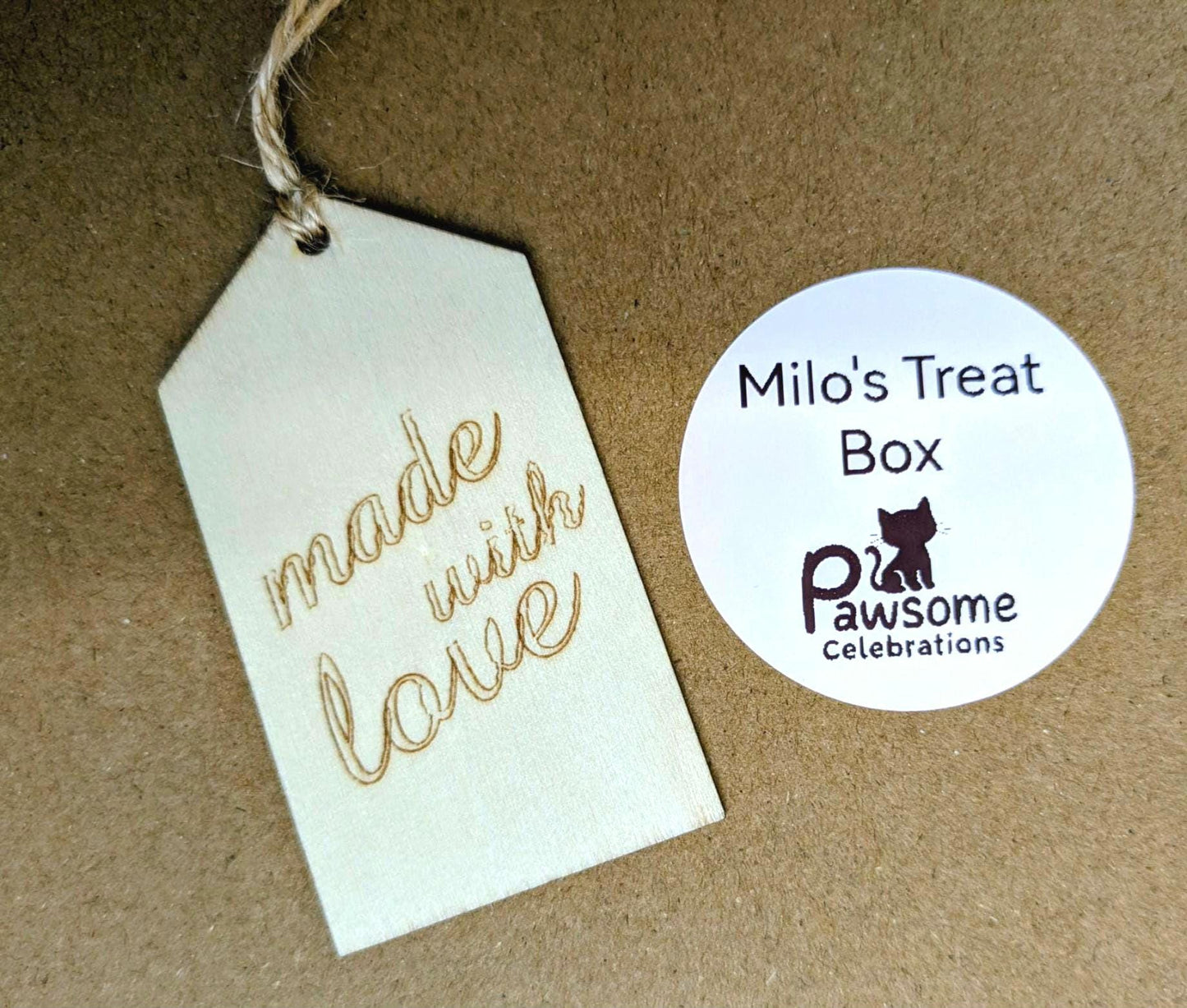Wooden tag engraved with "made with love" and personalized round label for Milo's Treat Box by Pawsome Celebrations on brown .