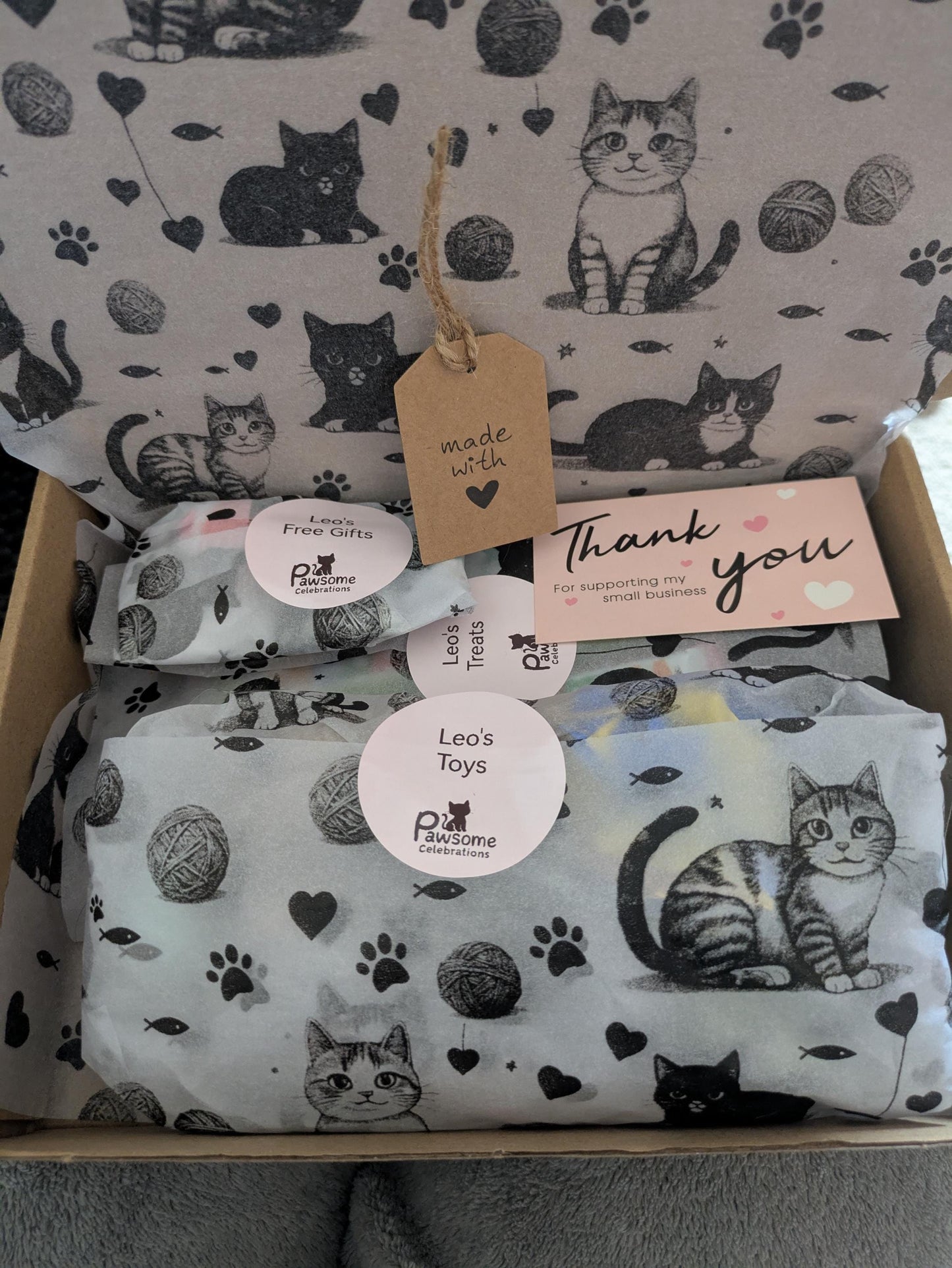 Open gift box filled with catnip kicker toy and packaged grain-free cat treats on cat-print tissue paper.