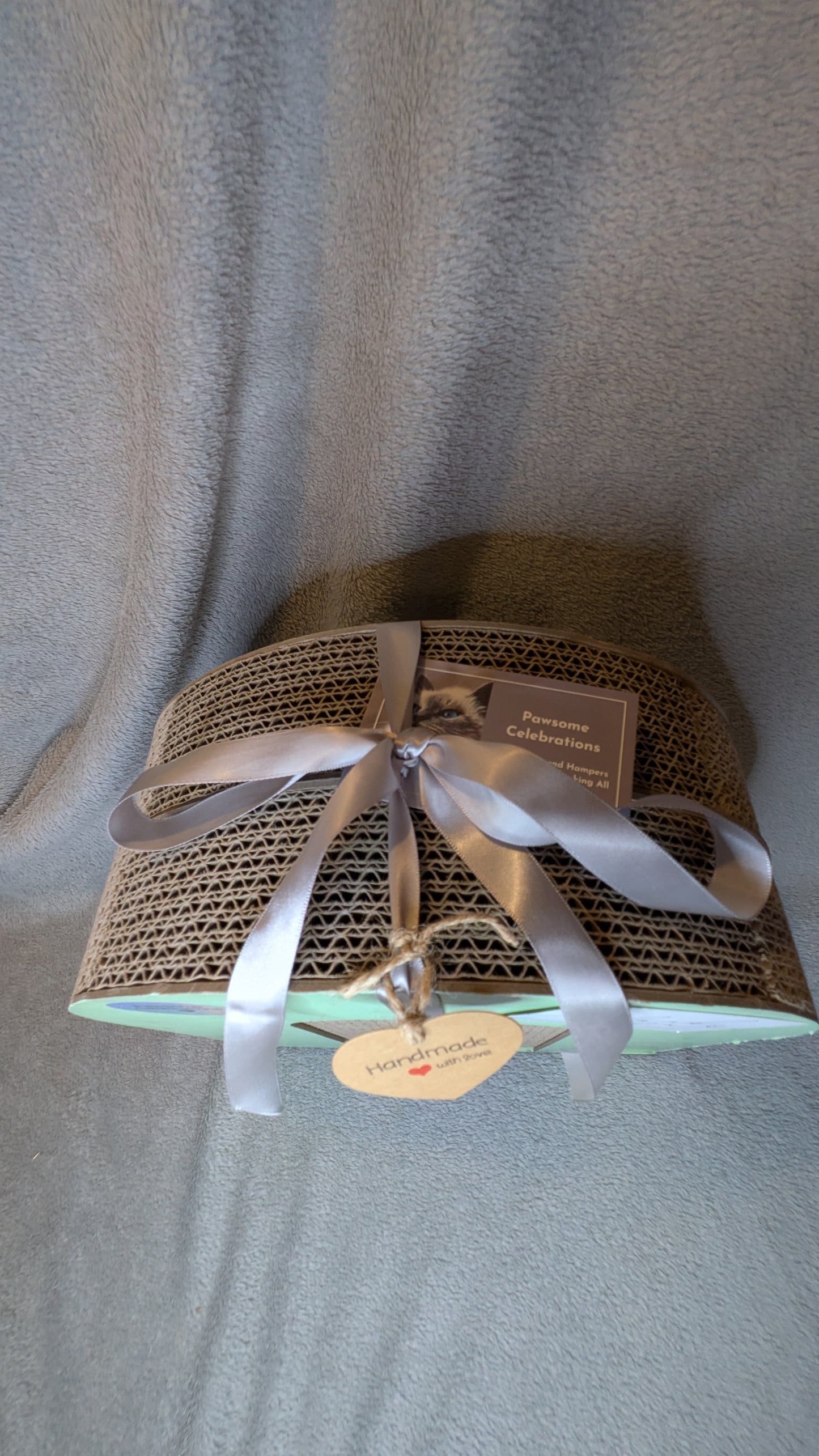 corrugated cardboard cat scratcher , presented with a ribbon on a grey fabric background