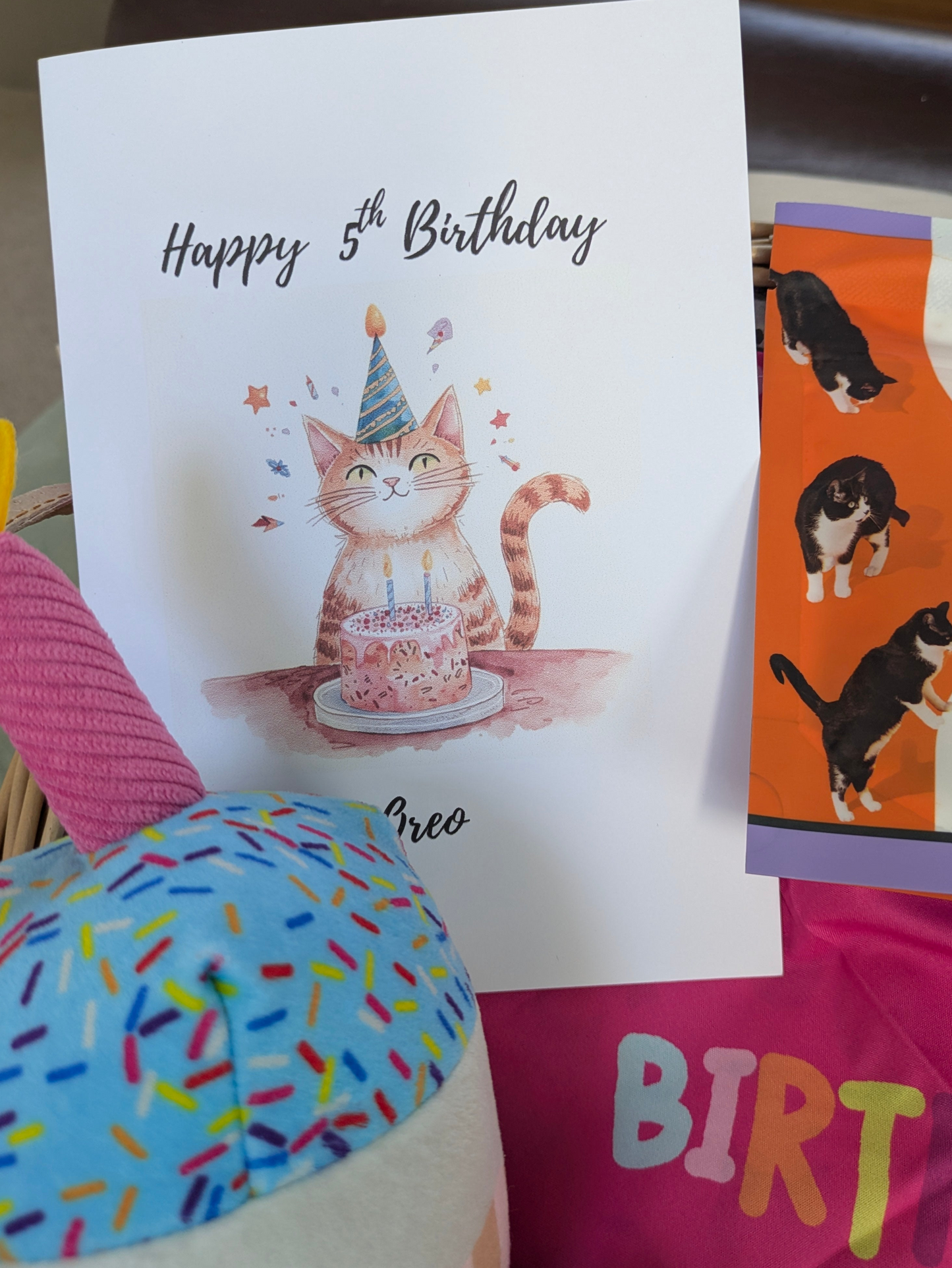 Birthday card with a cat illustration and text, surrounded by colorful items.