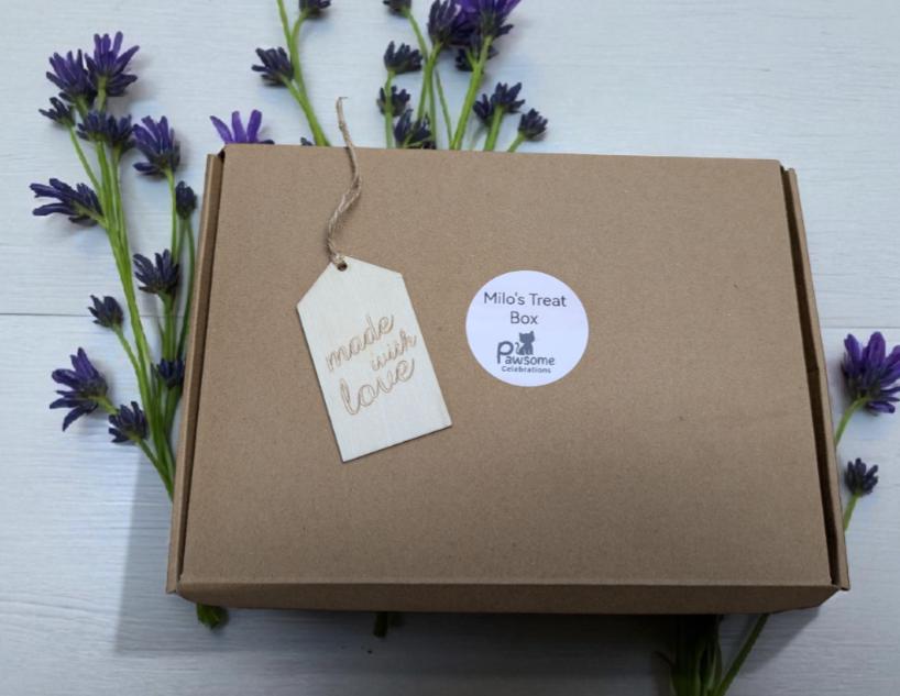 Brown eco-friendly cardboard gift box with white circular label and handwritten tag, surrounded by purple flowers.