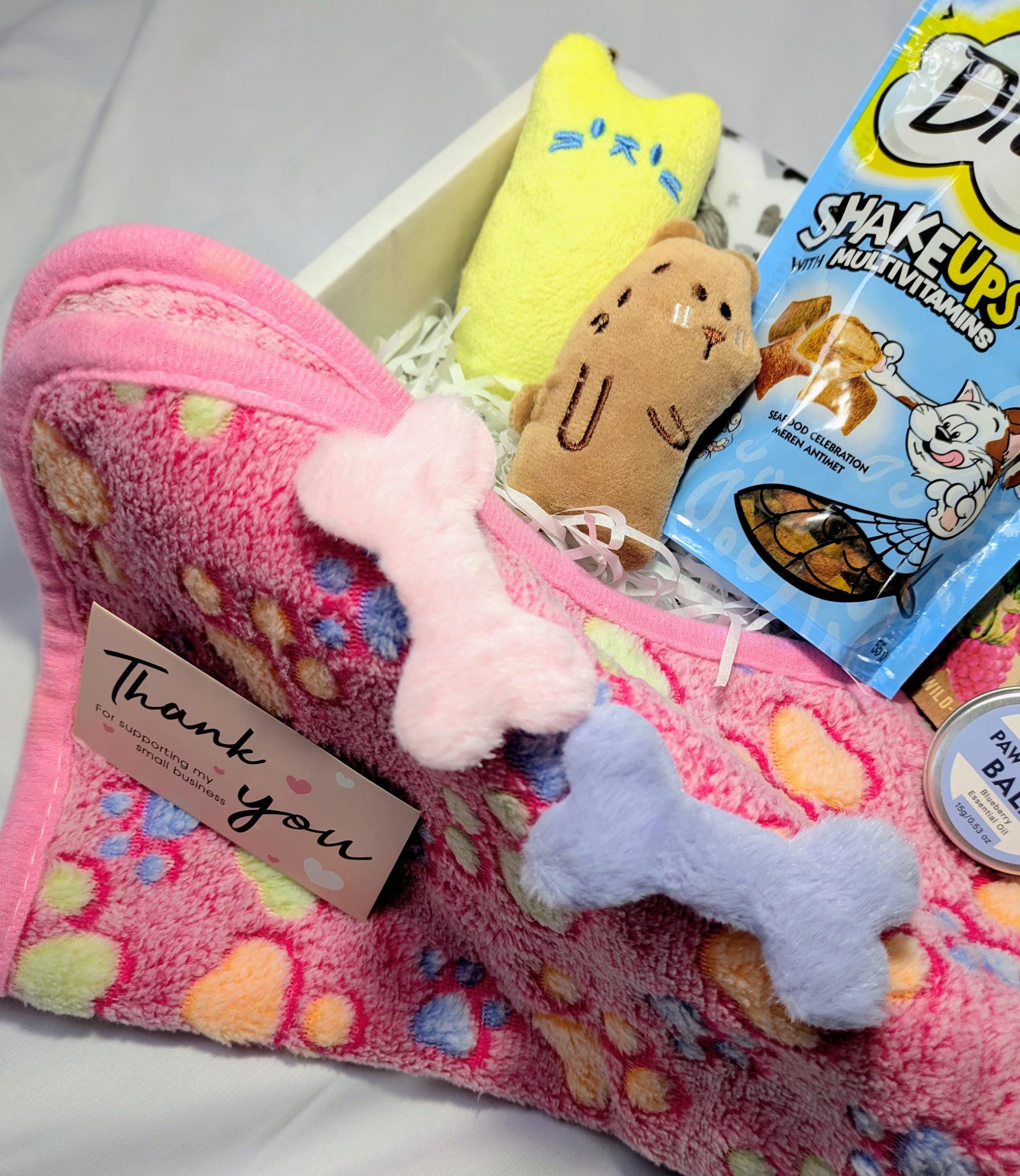 Pink polka dot soft cat blanket with two plush bone toys and a thank you card inside a white hamper box.