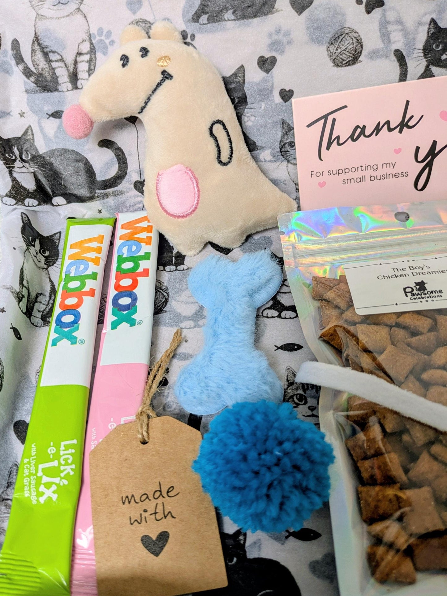 Personalised Mini Cat Treat Box with plush dog toy, blue pom-pom toy, catnip sticks, and natural cat treats in front of grey .