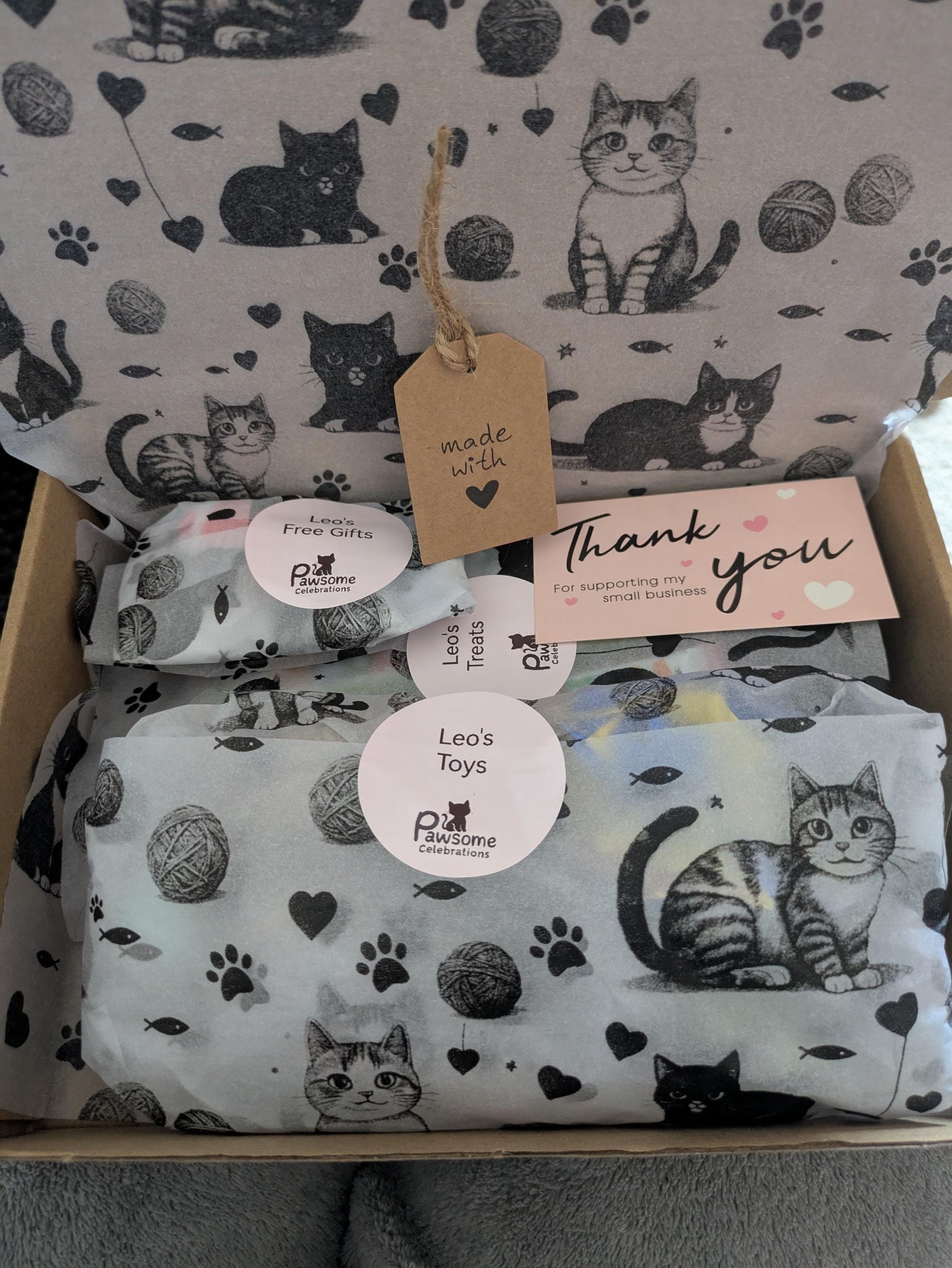 Open gift box filled with catnip kicker toy and packaged grain-free cat treats on cat-print tissue paper.