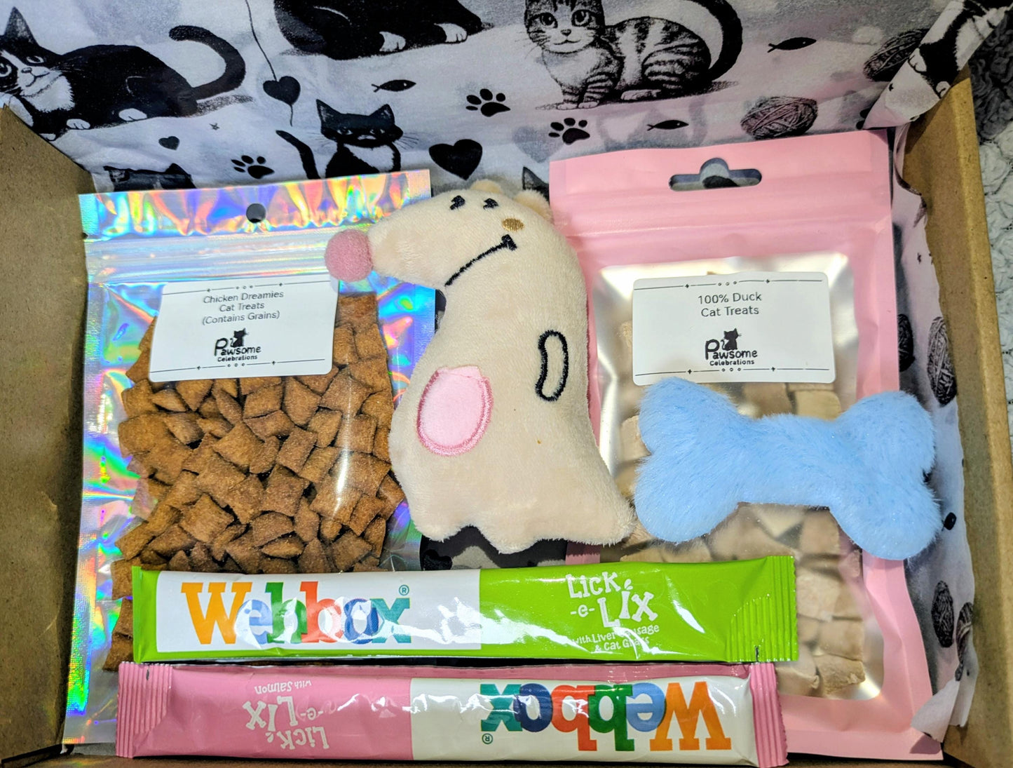 Small cat treat box with heart-shaped kibble, plush mouse toy, blue bone toy, and green and pink cat treat sticks in pink.