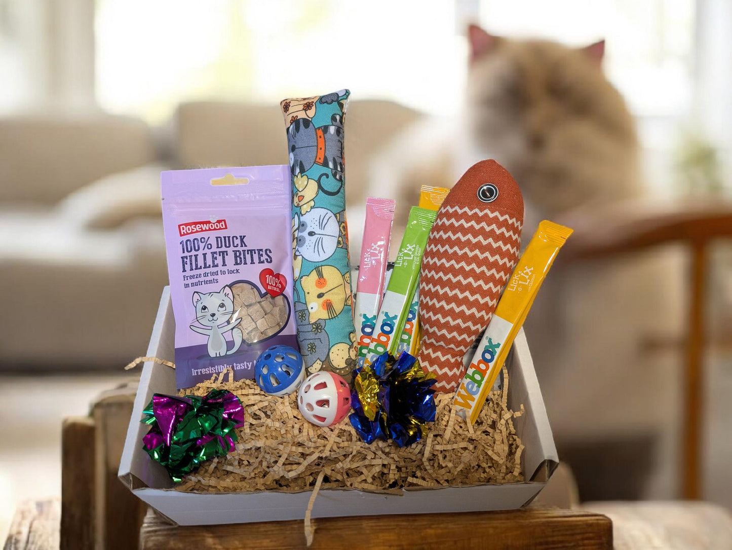 Wooden box filled with catnip toys and a bag of fish-flavored cat treats on straw bedding.