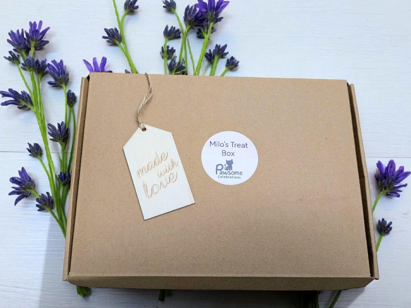 Brown cardboard gift box with "Mews Treat Box" tag and lavender flowers around.