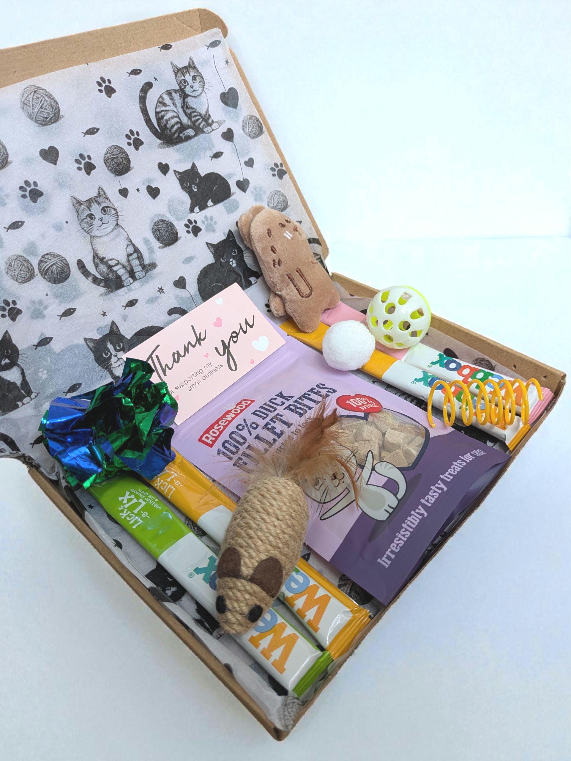 Open brown cardboard box with cat-themed tissue paper, catnip toys, and grain-free cat treat packets inside.