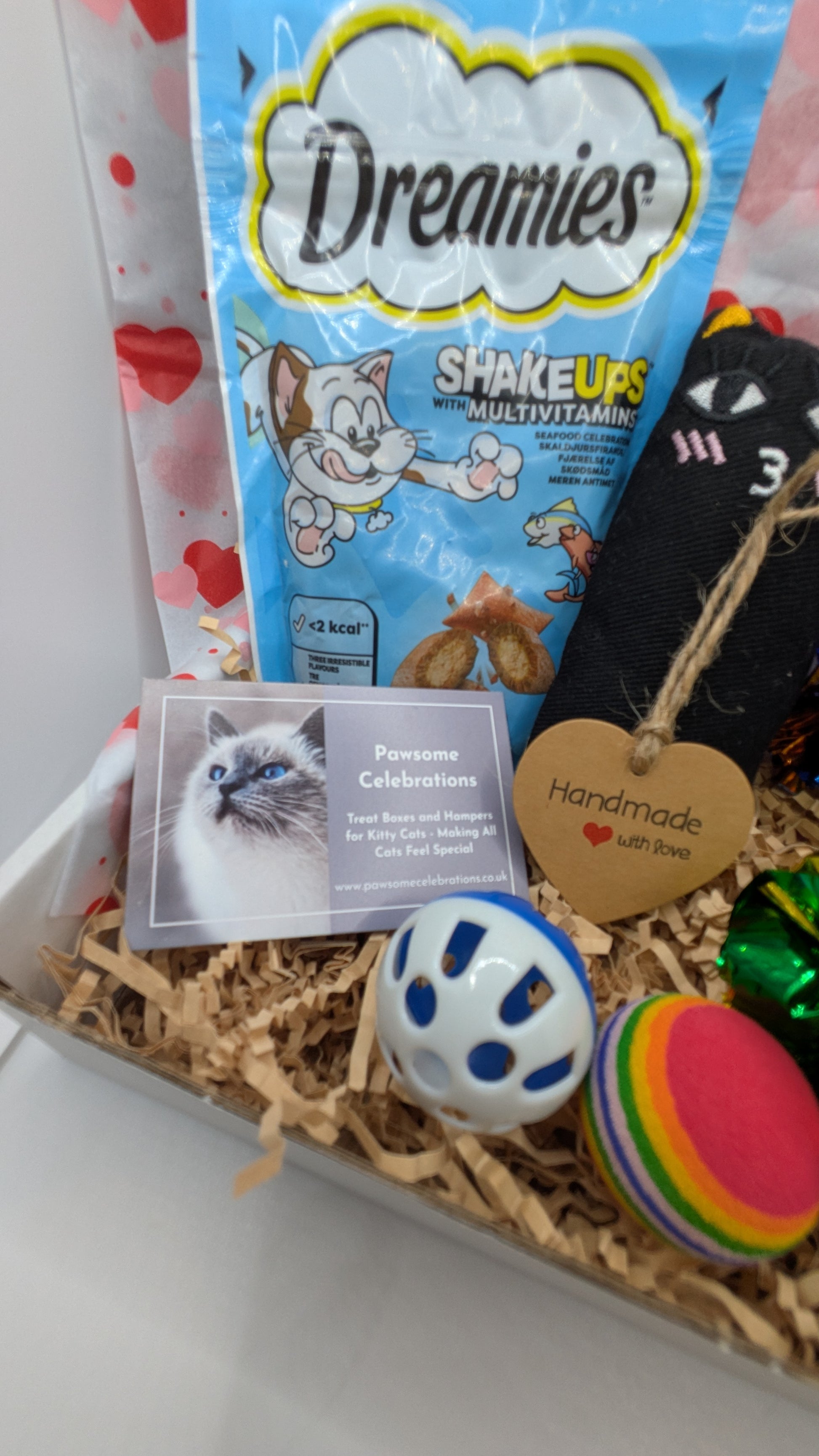 Cat-themed gift box with Dreamies cat treats, a photo of a cat, and pet toys.