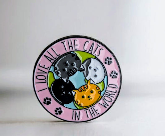 Enamel pin with cartoon cats and 'I love all the cats in the world' text on a pink background
