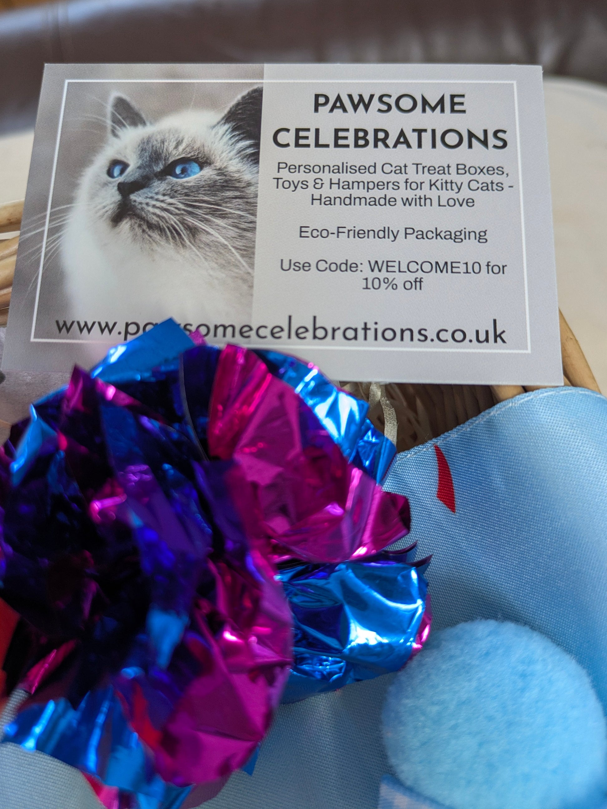 Promotional card for 'Pawsome Celebrations' with a cat and decorative items on a wooden surface.