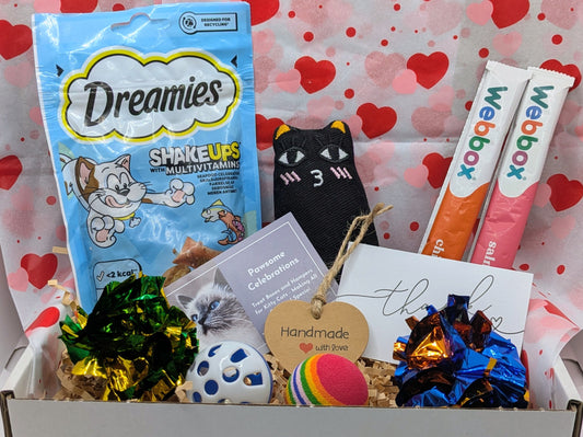 Cat-themed gift box with Dreamies cat treats, Weebly products, and decorative items on a heart-patterned background.