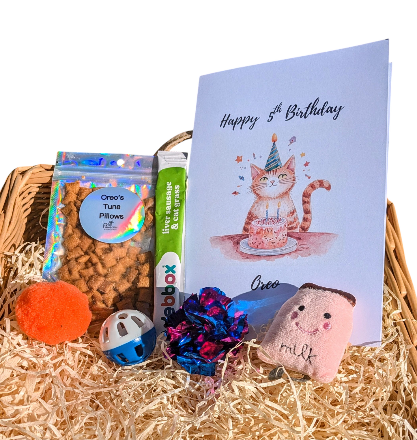 Cat-themed birthday gift basket with a card, toys, and treats on a white background