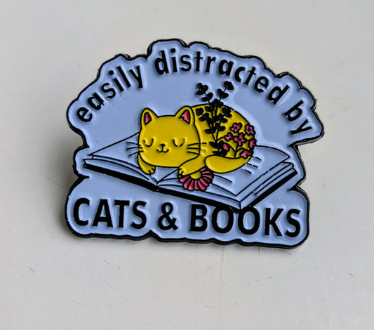 Enamel pin with a cat and book design and text 'easily distracted by cats & books' on a light background