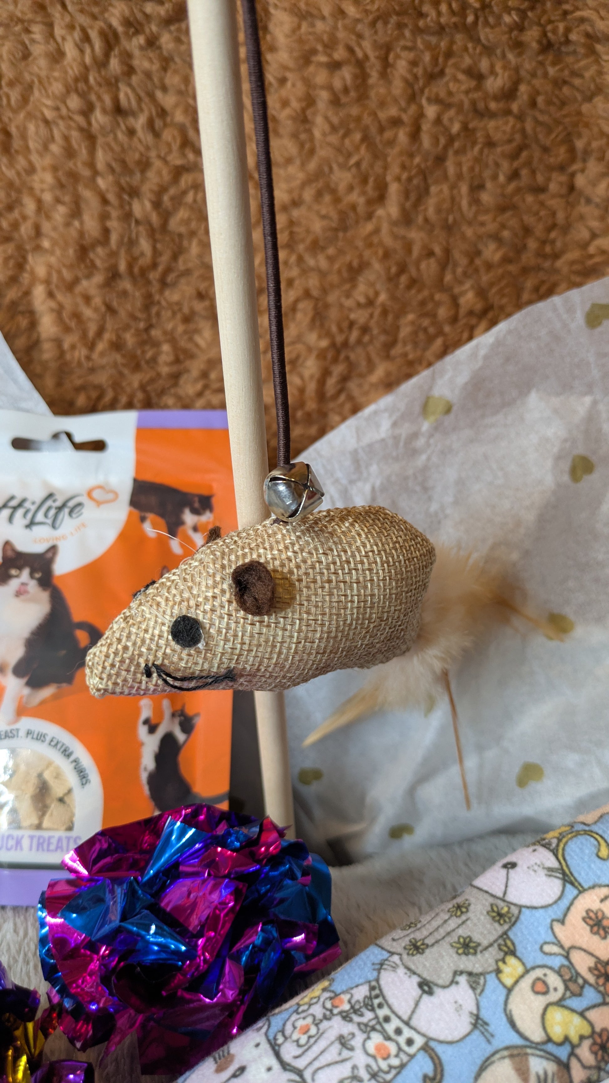 Textured mouse-shaped toy on a stick with a colorful ball, against a patterned background.