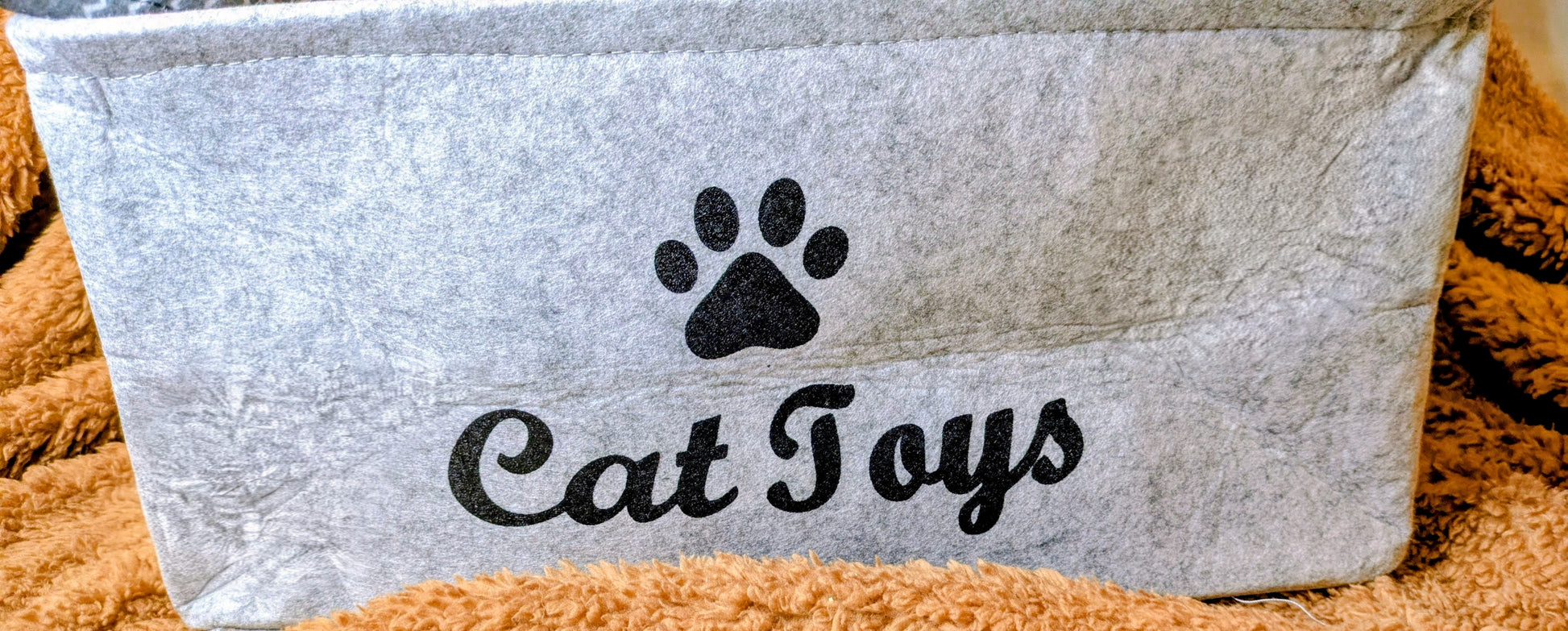 Grey basket labeled 'Cat Toys' with a paw print on a soft brown surface