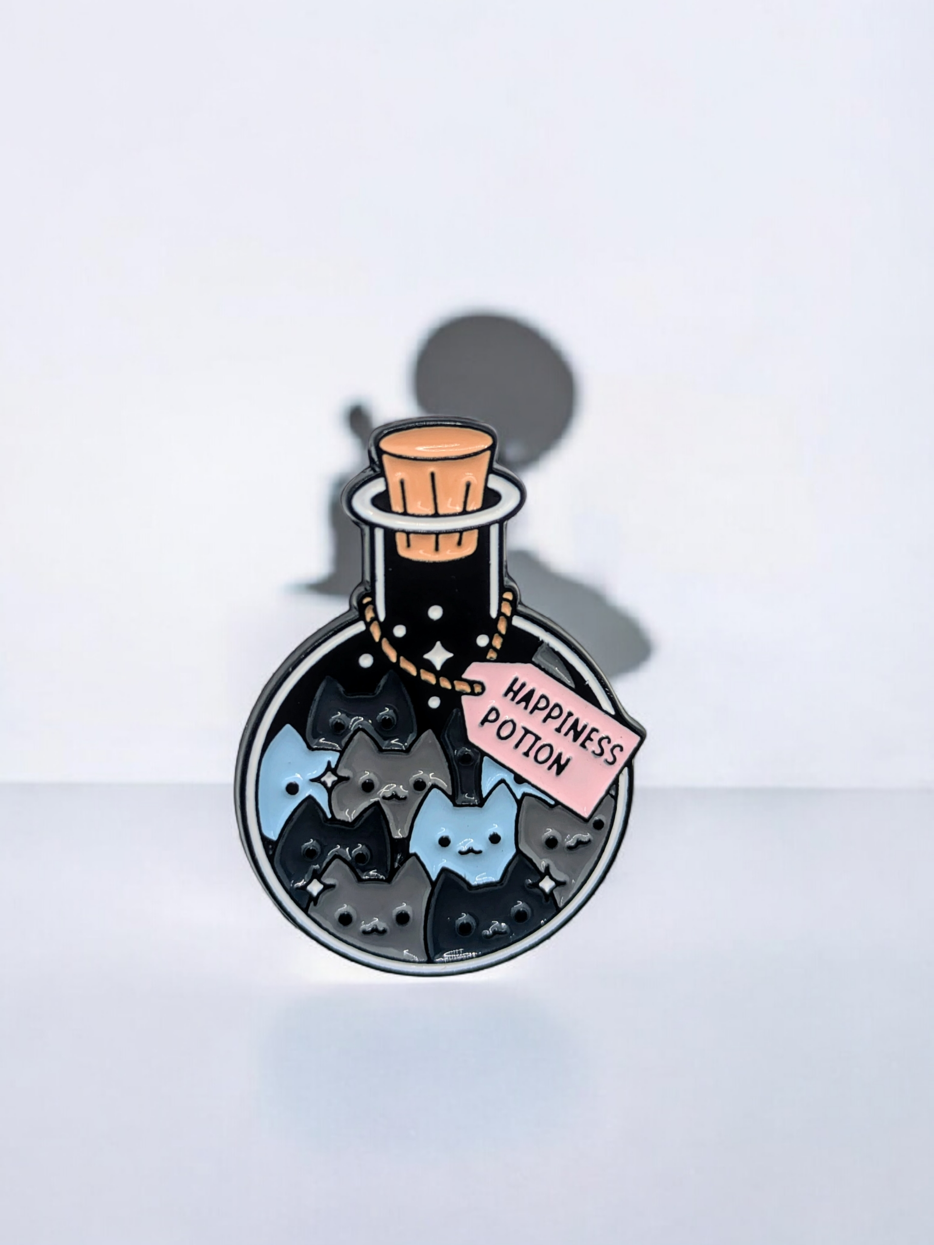 Enamel pin of a potion bottle labeled 'Happiness Potion' and it is filled with cats, on a white background