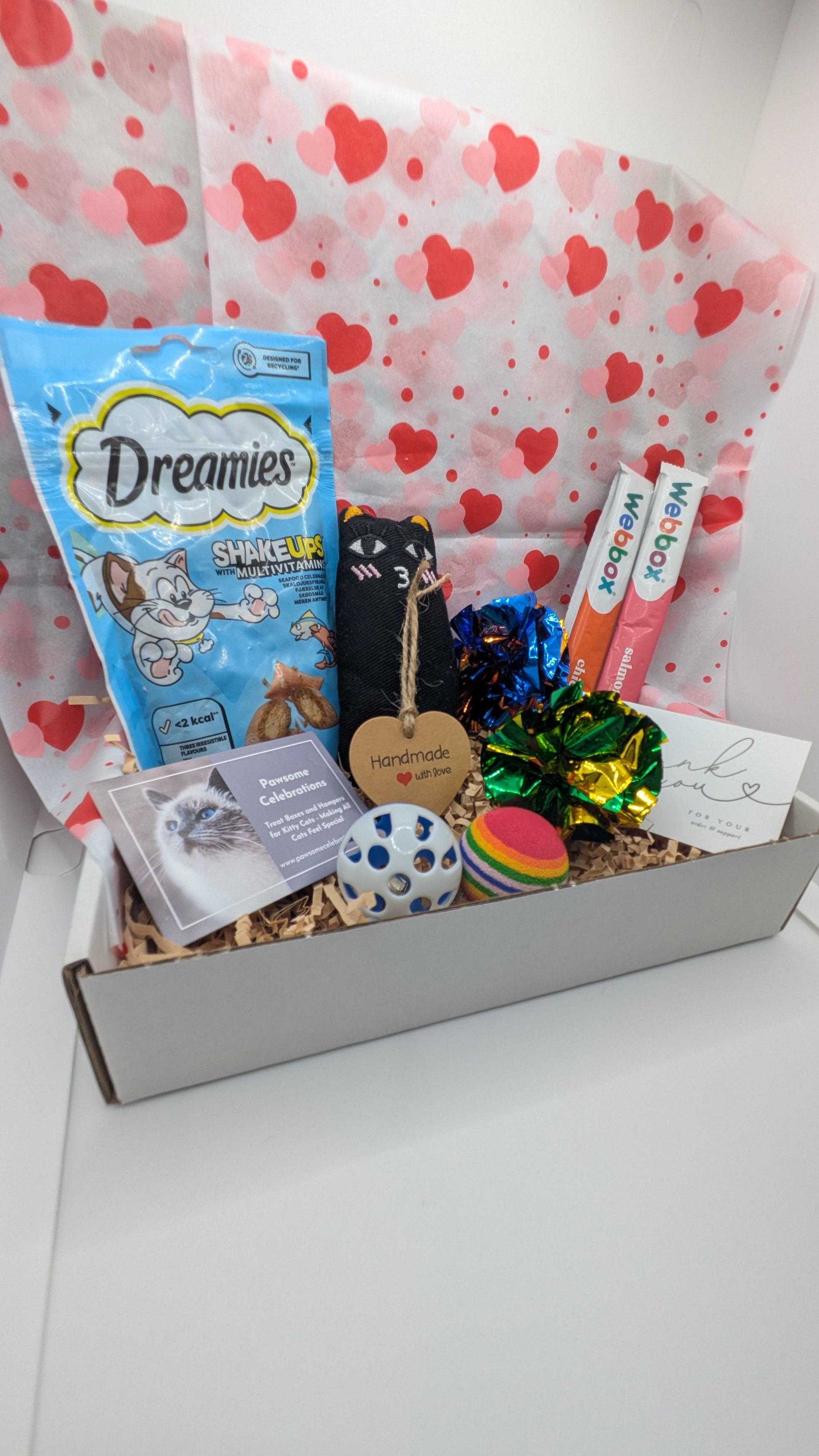 Cat gift box with various items including treats and toys on a heart-patterned background