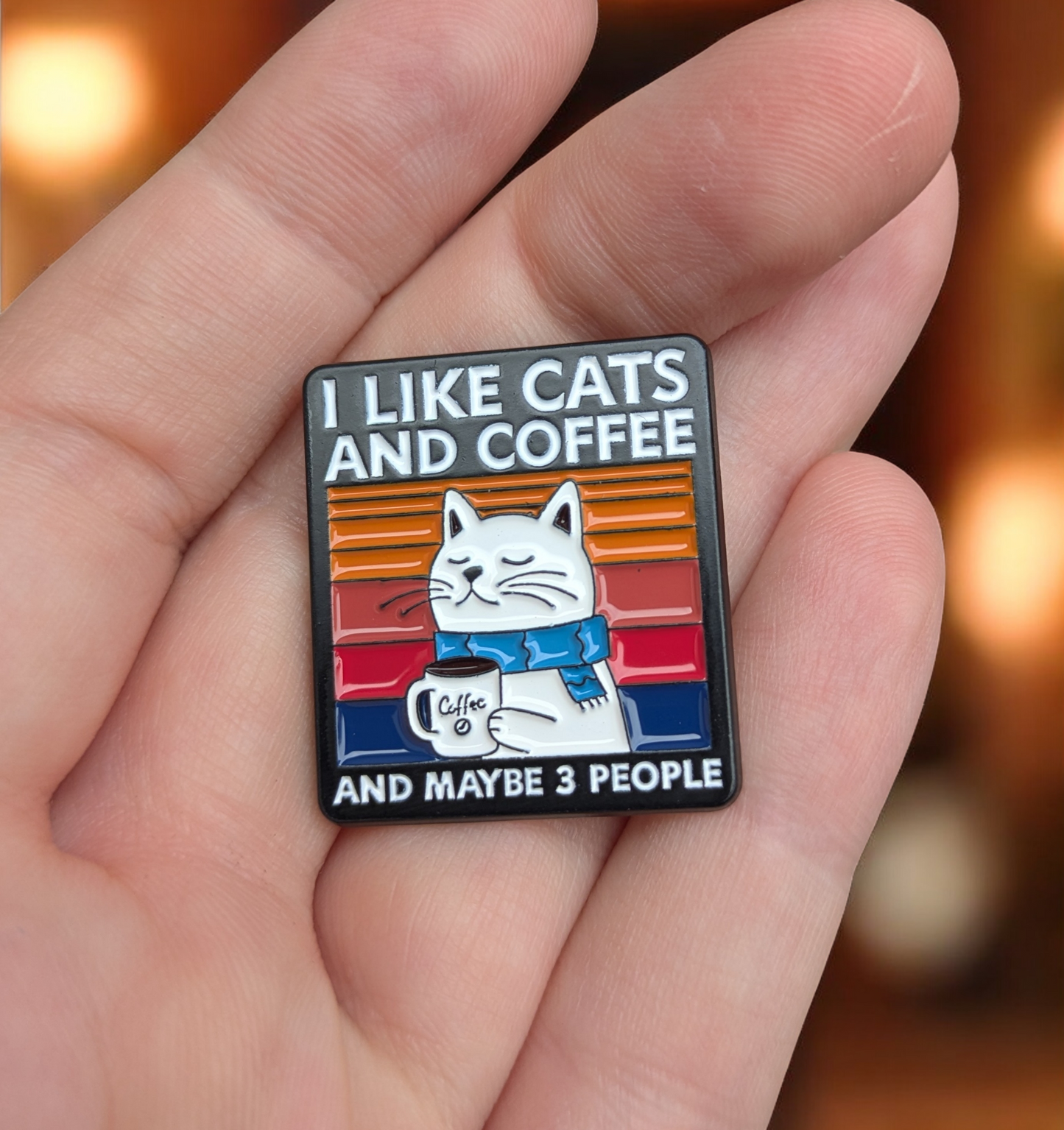 Enamel Pin with a cat and coffee design held in a hand against a blurred background