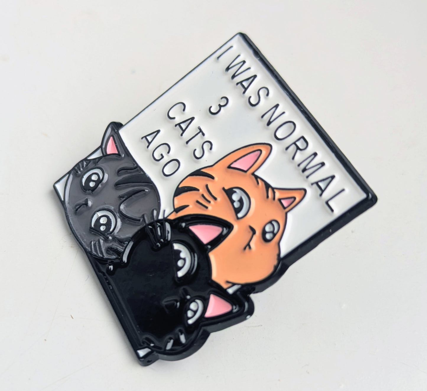 Enamel pin with cartoon cats and text 'I was normal 3 cats ago' on a white background
