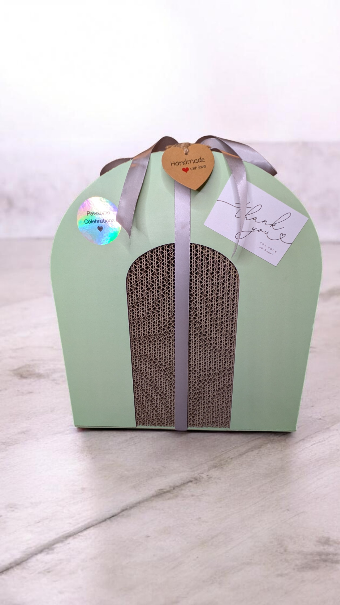 Mint Green cat scratcher interactive box with catnip balls, foldable, with brown ribbons and a tag on a white marble surface