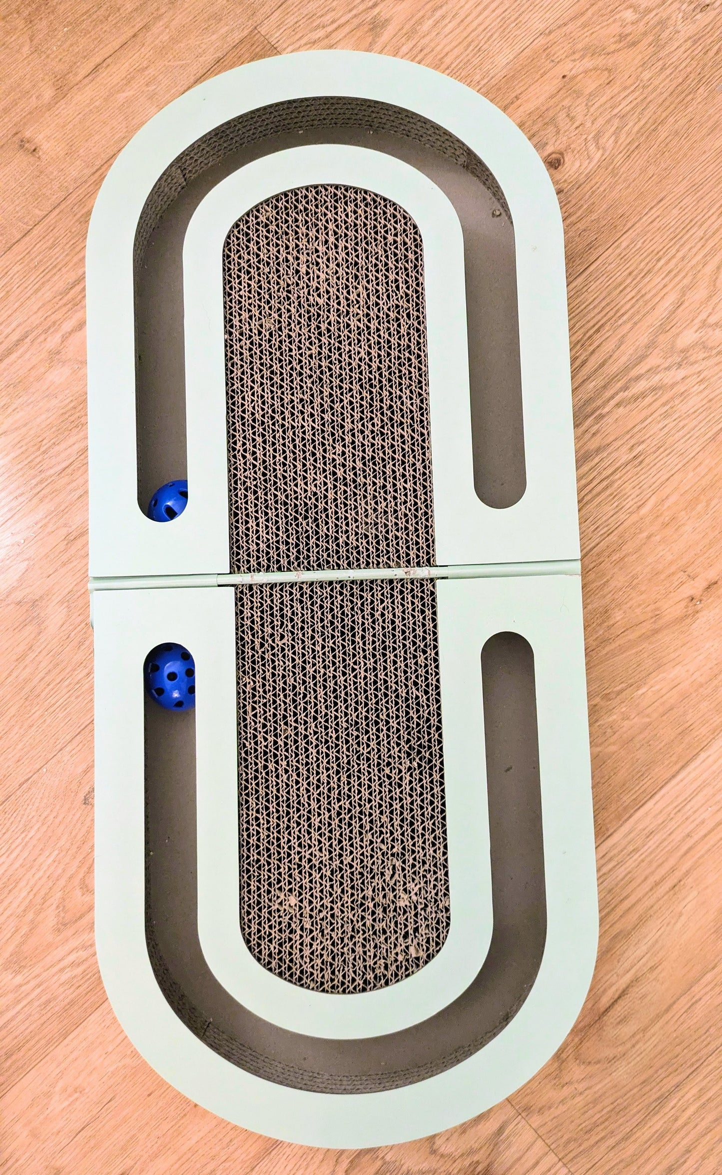 Rectangular cat scratcher pet toy with textured surface and blue balls with catnip on a wooden floor