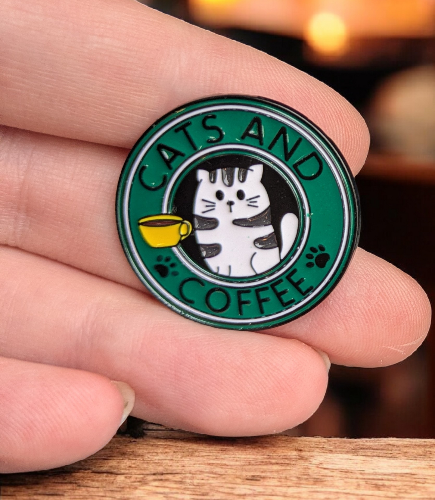 Pin with 'Cats and Coffee' design held between fingers