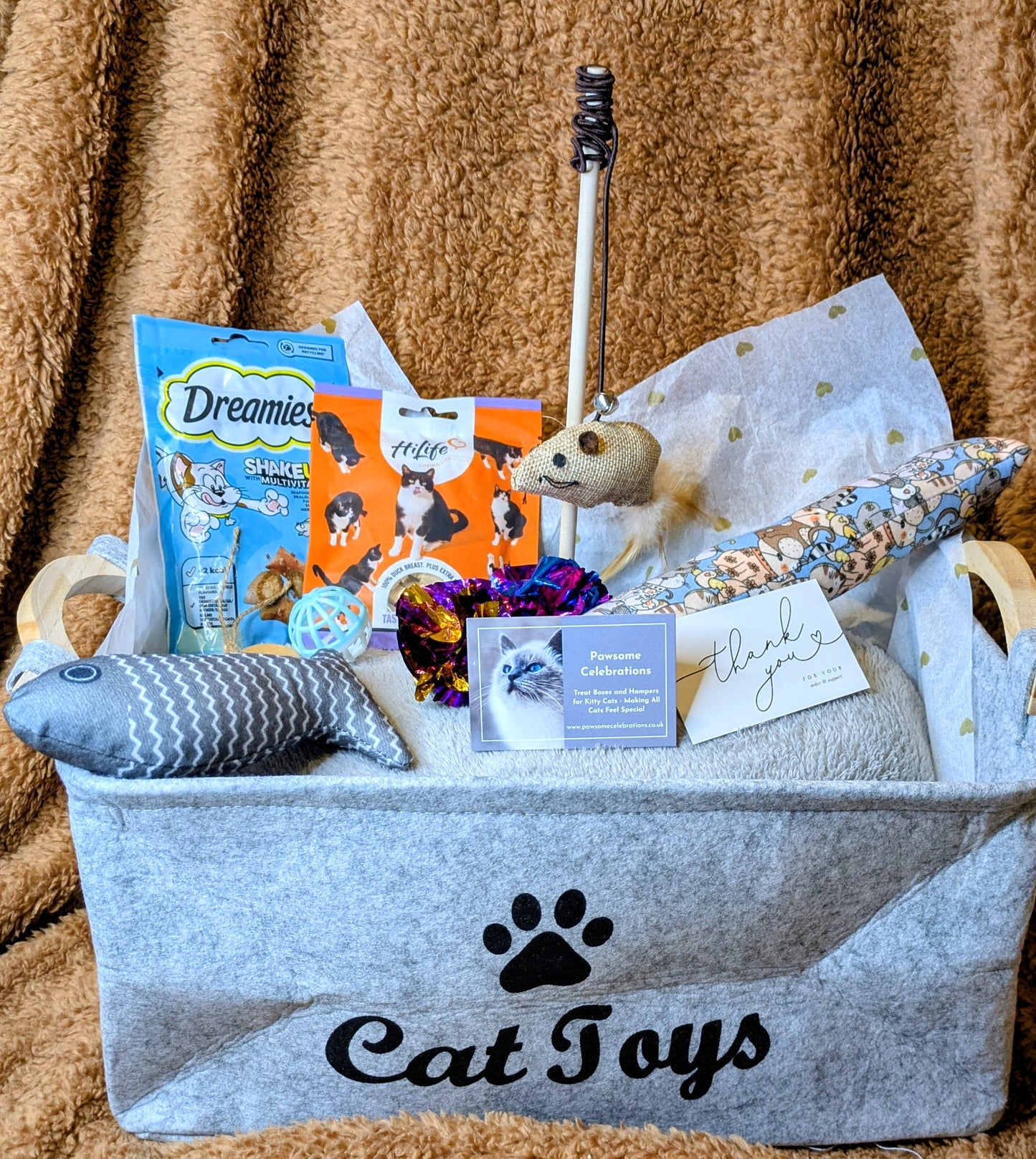 Cat toy basket with various cat toys and treats on a brown blanket