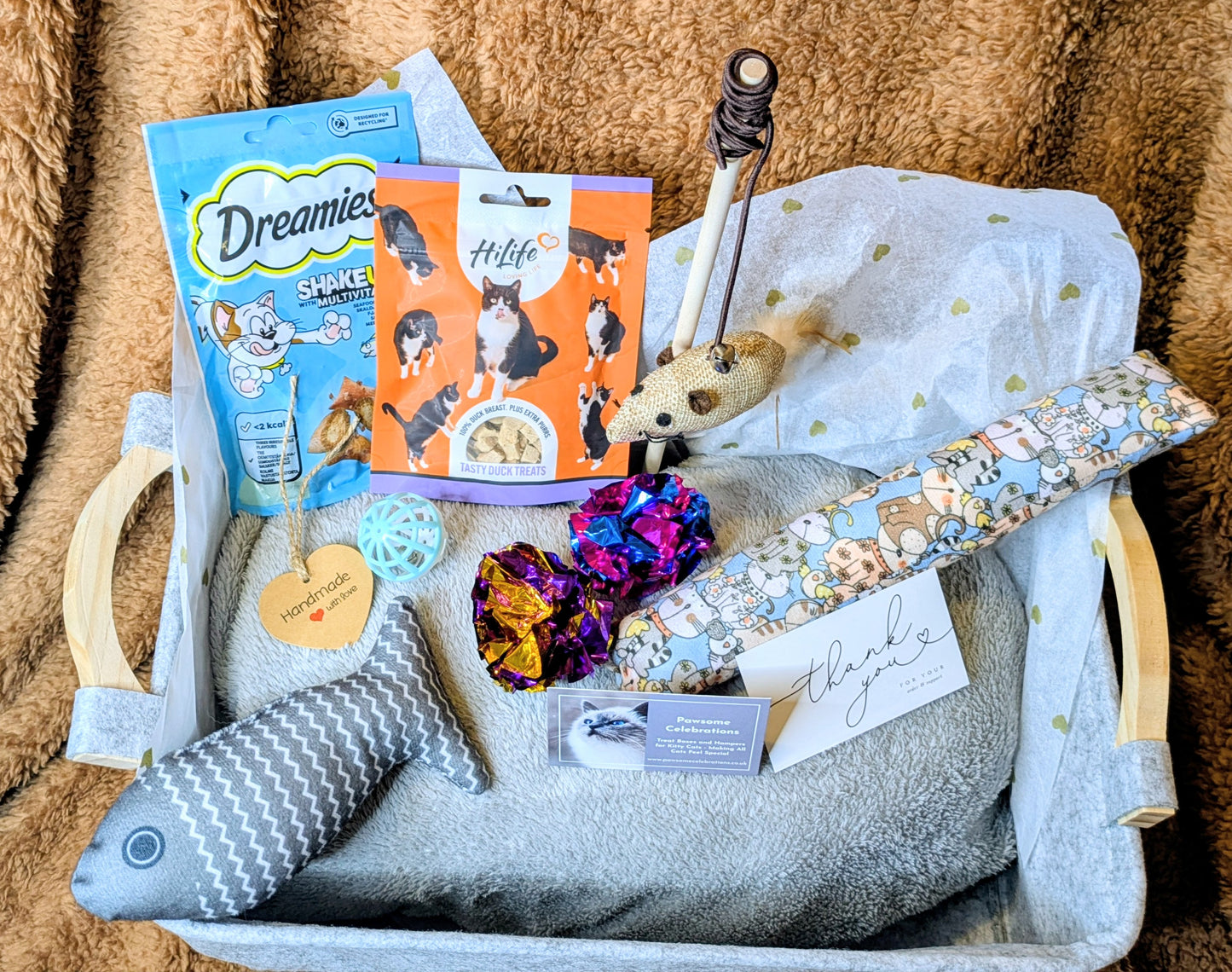 Cat toy box with dog toys, treats, and a plush fish toy on a brown blanket background.