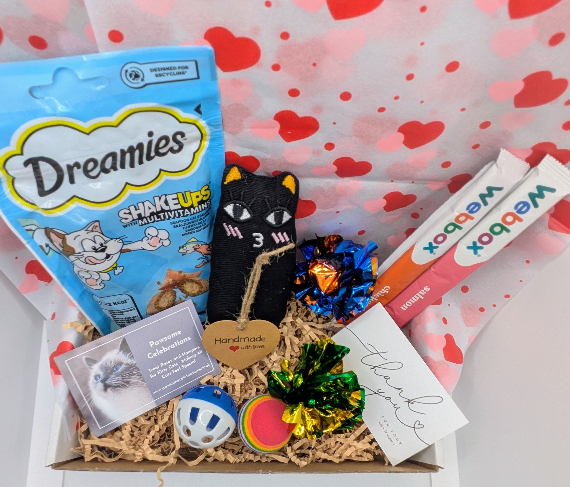 Cat-themed gift box with treats, toys, and cards on a heart-patterned background