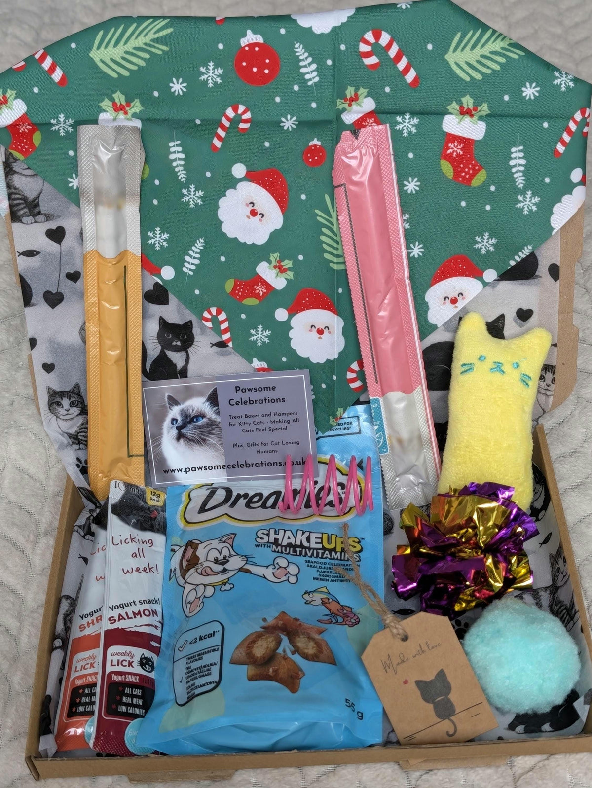 A curated pet gift box from Pawsome Celebrations, filled with treats, toys, and accessories. The box is lined with festive green Christmas-themed cat print paper.